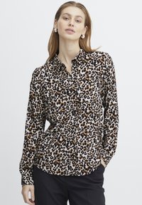 Blusa con stampa leopardata caratterizzata da maniche lunghe, chiusura con bottoni sul davanti, colletto e un tessuto leggero con sfumature di marrone, nero e crema.
