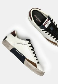 Baskets en cuir blanc avec des accents marron et noir, des superpositions texturées et une semelle en caoutchouc. Présente des lacets noirs et un détail de logo.