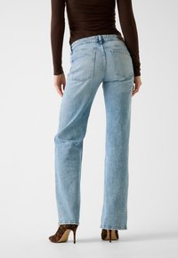 Jeans in denim azzurro chiaro con design a gamba dritta, tasche visibili e una discreta toppa con logo sul retro. Indossati con tacchi alti decorati.