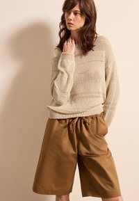 Beige Strickpullover mit strukturiertem Muster, kombiniert mit lockeren braunen Shorts mit elastischem Bund und gebundenem Kordelzug.
