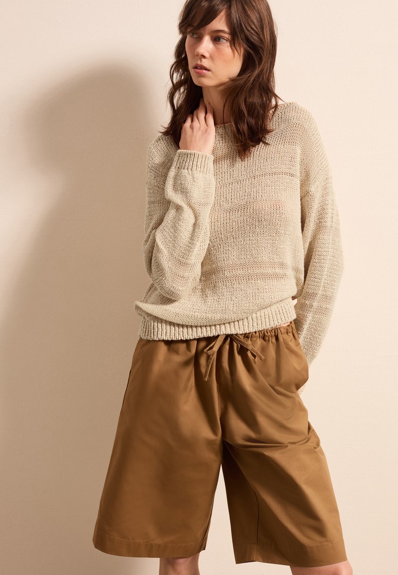 Beige Strickpullover mit strukturiertem Muster, kombiniert mit lockeren braunen Shorts mit elastischem Bund und gebundenem Kordelzug.