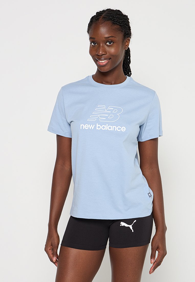 Helles blaues Baumwoll-T-Shirt mit weißem "New Balance"-Logo, kombiniert mit schwarzen Shorts, die ein weißes Puma-Logo zeigen. Kurzärmlig, runder Ausschnitt.