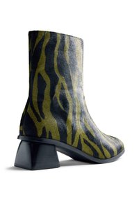 Bota de tobillo con un patrón de rayas de cebra en negro y verde oliva, tacón cuadrado y grueso, y suela lisa.