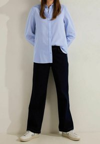 Ljusblå skjorta med knappar och långa ärmar, kombinerad med mörkblå vida jeans och vita sneakers med grå detaljer.