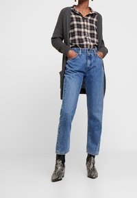 Cardigan grigio a maglia, camicia a quadri bianca e nera, jeans dritti blu e stivaletti alla caviglia in pelle di serpente nera e grigia.