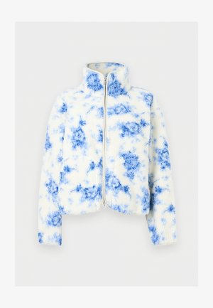 Weiße Fleecejacke mit blauen Batikmustern, einem durchgehenden Frontreißverschluss und einem Stehkragen, vor einem einfarbigen Hintergrund präsentiert.