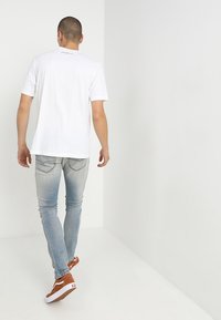 Camiseta blanca de manga corta con cuello redondo, combinada con jeans de mezclilla azul claro y zapatillas marrones con suelas blancas.