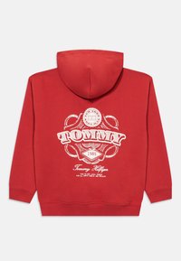 Κόκκινη φούτερ μπλούζα με κουκούλα και άσπρο λογότυπο Tommy Hilfiger σε vintage στυλ, καθώς και κείμενο "1985" εκτυπωμένο στην πλάτη. Ριμπά μανίκια και στρίφωμα.