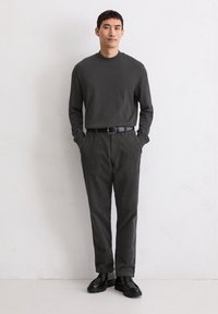 Długi rękaw ciemnoszarej bluzki, zestawiony z czarnymi spodniami w prążki oraz czarnymi sznurowanymi butami. Codzienny fason o luźnym kroju.