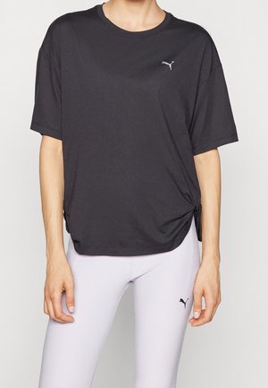 Persoon draagt een losse zwarte Puma T-shirt met een klein logo en aansluitende witte Puma legging met logo op de dij.