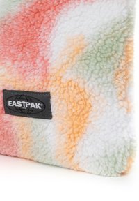 Chlupatý, vícebarevný textil se vzory v oranžové, růžové, zelené a bílé barvě; zahrnuje černou etiketu EASTPAK s logem globu.