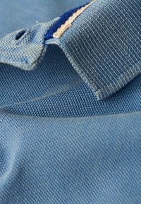 Tessuto in denim blu con una trama testurizzata, caratterizzato da un colletto ripiegato e dettagli cuciti in blu navy e rosa chiaro.