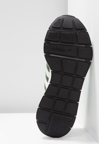 Svart gummisul med ett flexibelt rutmönster, med gröna och vita detaljer längs de övre kanterna och logotyp på sidan.