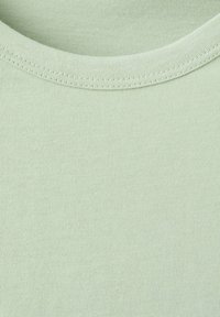 Tissu en coton vert clair avec gros plan sur l'encolure ronde et couture double.