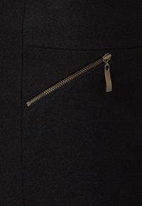 Svart tyg med en dragkedjeficka med en guldfärgad dragkedja. Texturen verkar slät och mjuk, vilket framhäver designens enkelhet.