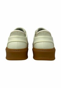 Zapatillas de cuero blancas con forma redondeada y suela de goma marrón; cuentan con costuras verticales y un diseño acolchado.