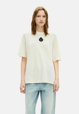 T-shirt bianco a maniche corte in mesh con un design ricamato nero sul colletto. Abbinato a jeans azzurri a vita alta.