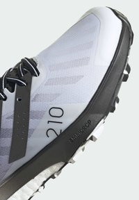 Zapatilla de trail running con una parte superior de malla gris ligera, acentos negros, suela de goma texturizada y cap toe reforzada para mayor durabilidad.