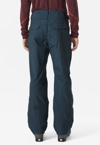 Navy waterdichte skibroeken met elastische tailleband, versterkte onderzoom en twee achterzakken. Getextureerde stof en logo-detail zichtbaar.
