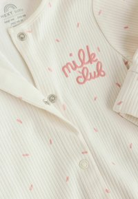 Valkoinen ribbikangas vauvan body, jossa vaaleanpunainen nonparellikuvio ja rinnan kohdalla kirjailtu teksti "milk club", jossa painonapit.
