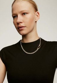 Collar de cadena de plata con un diseño de eslabones gruesos, con un cierre en tono dorado, que se lleva sobre una blusa negra ajustada.