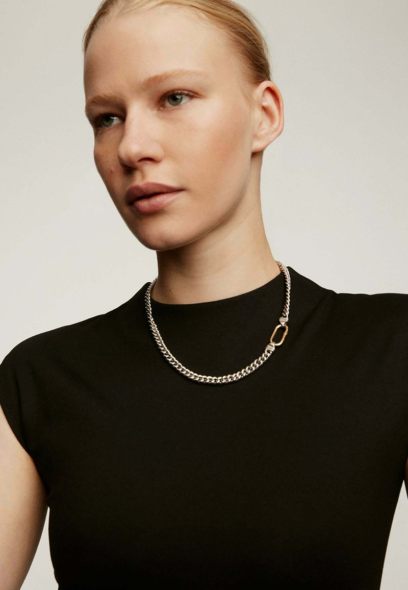 Collar de cadena de plata con un diseño de eslabones gruesos, con un cierre en tono dorado, que se lleva sobre una blusa negra ajustada.
