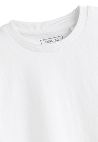 Gros plan d'un t-shirt blanc en coton à col rond montrant un col côtelé et une étiquette intérieure avec la marque Next et la taille 82.