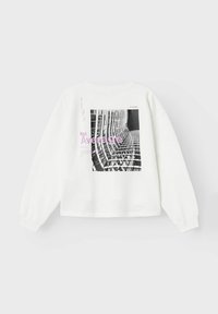 Sudadera blanca con un gran gráfico en blanco y negro de un edificio y el texto "Not Average" en púrpura. Tiene un corte relajado y cuello redondo.