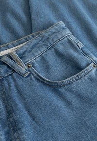 Jeans in denim blu chiaro con un classico design a cinque tasche, cuciture visibili e un bottone in metallo argentato sulla vita.