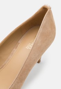 Chaussure à talon aiguille en suédine beige avec un bout pointu et un talon effilé. L'intérieur est doté d'un revêtement lisse. Le logo de la marque est embossé sur la semelle intérieure.