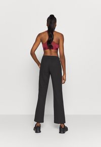 Sportovní outfit zahrnující vínovou sportovní podprsenku s designem racerback a černé volné kalhoty. Kalhoty mají elastický pas.