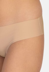 Beige nahtlose Hipster-Unterwäsche mit glatter Textur und breitem Bund, vor einem neutralen Hautton-Hintergrund dargestellt.