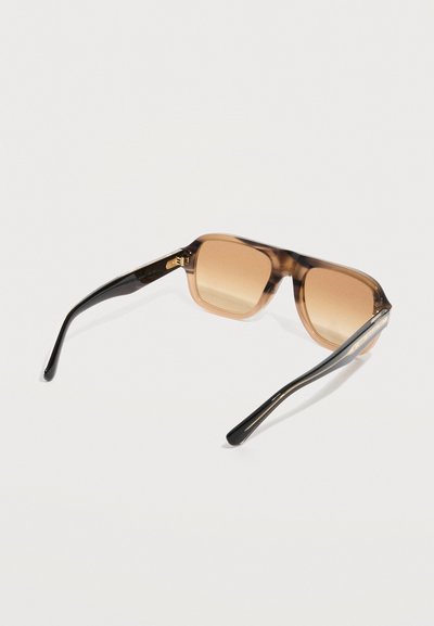 Καφέ αποχρωματισμένα ορθογώνια γυαλιά ηλίου με διαφανή καφέ και μαύρα πλαίσια, ανοιχτά και τοποθετημένα πάνω σε λευκή επιφάνεια.