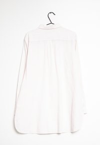 Camicia a maniche lunghe rosa chiaro con colletto, caratterizzata da strisce verticali, una piega sul retro e un orlo curvo, appesa a un gancio nero.