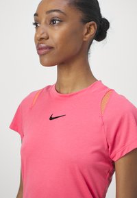 Top deportivo rosa con mangas cortas, logotipo de Nike en negro y acentos de malla naranja en los hombros. Textura suave y diseño ajustado.
