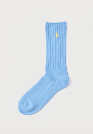 Light blue ribbed sock with yellow embroidered polo player logo near the top, laid flat on a white background.