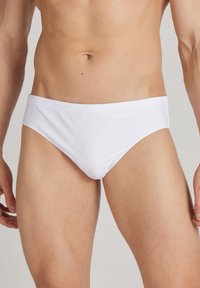 Weiße Schwimmbörsen mit einer glatten Textur und einem niedrigen Schnitt, die einen minimalistischen Stil und einen elastischen Bund aufweisen.