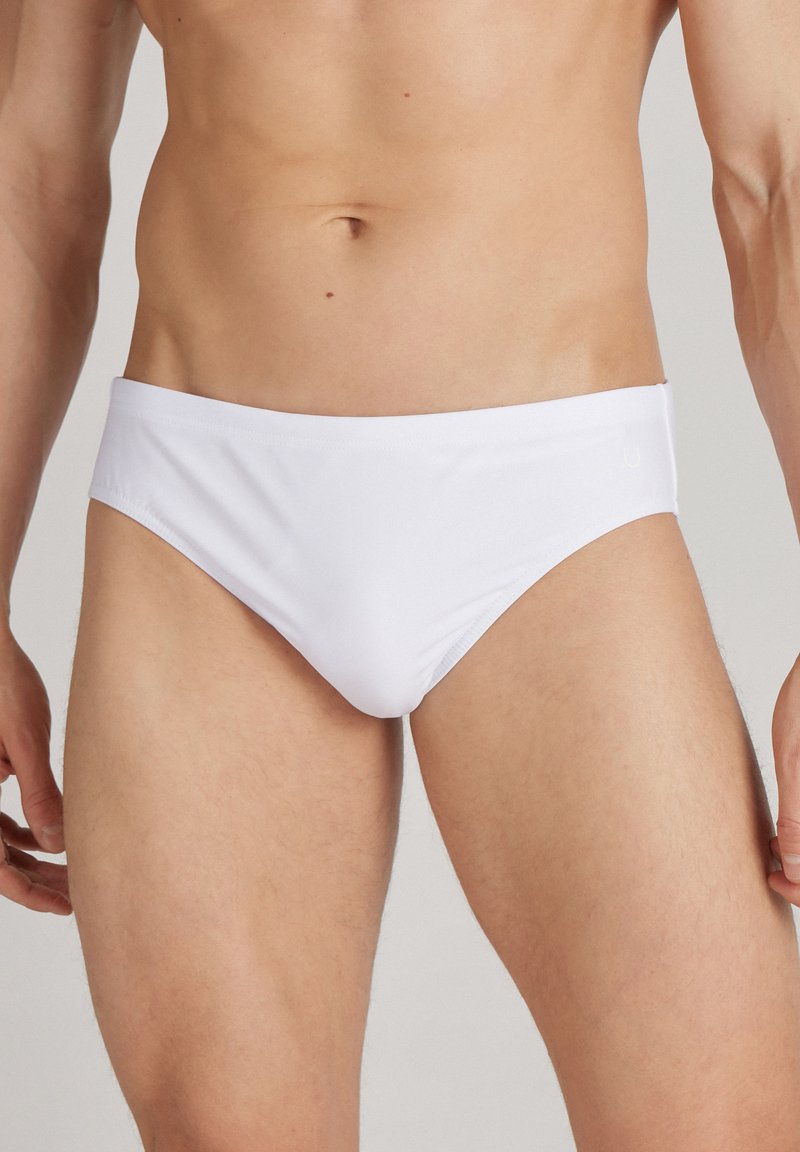 Weiße Schwimmbörsen mit einer glatten Textur und einem niedrigen Schnitt, die einen minimalistischen Stil und einen elastischen Bund aufweisen.
