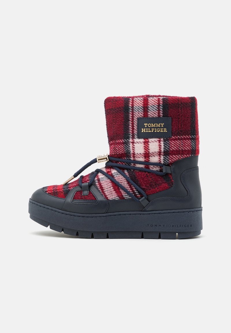 Bota de invierno a cuadros rojos y marinos con suela gruesa en color marino y cordones, que presenta un parche con el logo de Tommy Hilfiger en la parte superior.