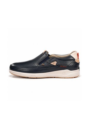 Zapatilla deportiva de cuero negra con cierre tipo slip-on, detalles en beige y rojo, paneles laterales elásticos y suela de goma blanca, mostrada sobre fondo blanco.