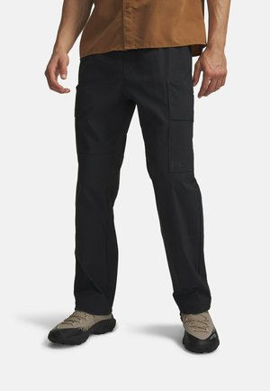 Black cargo pants with multiple pockets, a straight leg design, crafted from textured fabric, paired with lightweight gray hiking shoes.