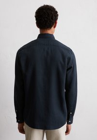 Dunkelblaues Hemd mit langen Ärmeln, klassischem Kragen und Knöpfen an den Manschetten. Glatte Textur und lockerer Schnitt, mit einem leicht abgerundeten Saum.