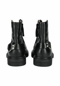 Bottines en cuir noir avec une finition lisse, zip à l'arrière et une sangle réglable avec boucle décorative en argent. Semelle extérieure en caoutchouc plate.