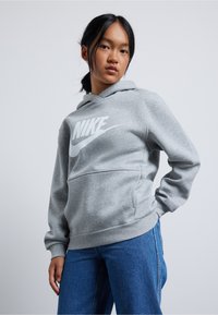 Pilkas džemperis su kapuche, pagamintas iš minkštos medžiagos, su dideliu baltu Nike logotipu priekyje. Įeina kengūros kišenė ir susiraukšlėjusi apykaklė bei kraštas.