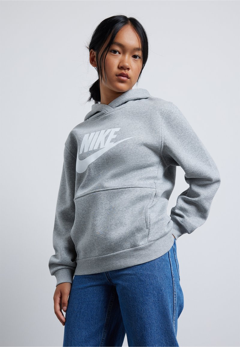 Pilkas džemperis su kapuche, pagamintas iš minkštos medžiagos, su dideliu baltu Nike logotipu priekyje. Įeina kengūros kišenė ir susiraukšlėjusi apykaklė bei kraštas.