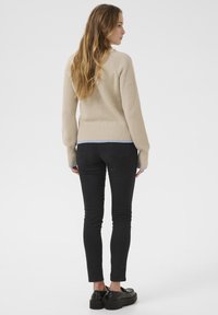 Beige neulepaita, jossa on ribattu helma ja vaaleansiniset hihansuut, yhdistetty mustiin slim fit -farkkuihin ja paksuihin mustiin kenkiin.