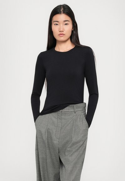 Long-sleeve black top with a round neckline, made of smooth fabric, paired with light gray patterned trousers featuring a loose fit and pleats.