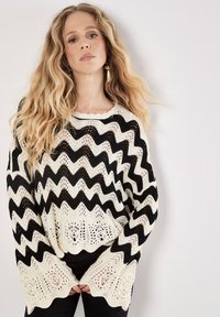 Gestreifter, schwarzer und cremfarbener, gestrickter Pullover mit Zickzackmuster, offenem Strickmuster, rundem Ausschnitt und weiten Ärmeln. Lässiger, lockerer Schnitt.