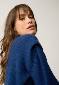 Niebieski, dziany sweter o prążkowanej fakturze i szerokich rękawach. Charakteryzuje się luźnym krojem oraz miękkim, grubym materiałem.