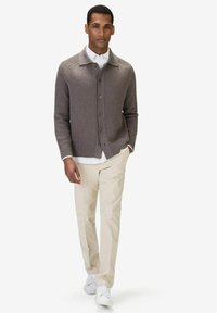 Stickad kofta i taupe, med knappframsida, ribbad struktur och kragdesign, parat med beige byxor och vita sneakers.